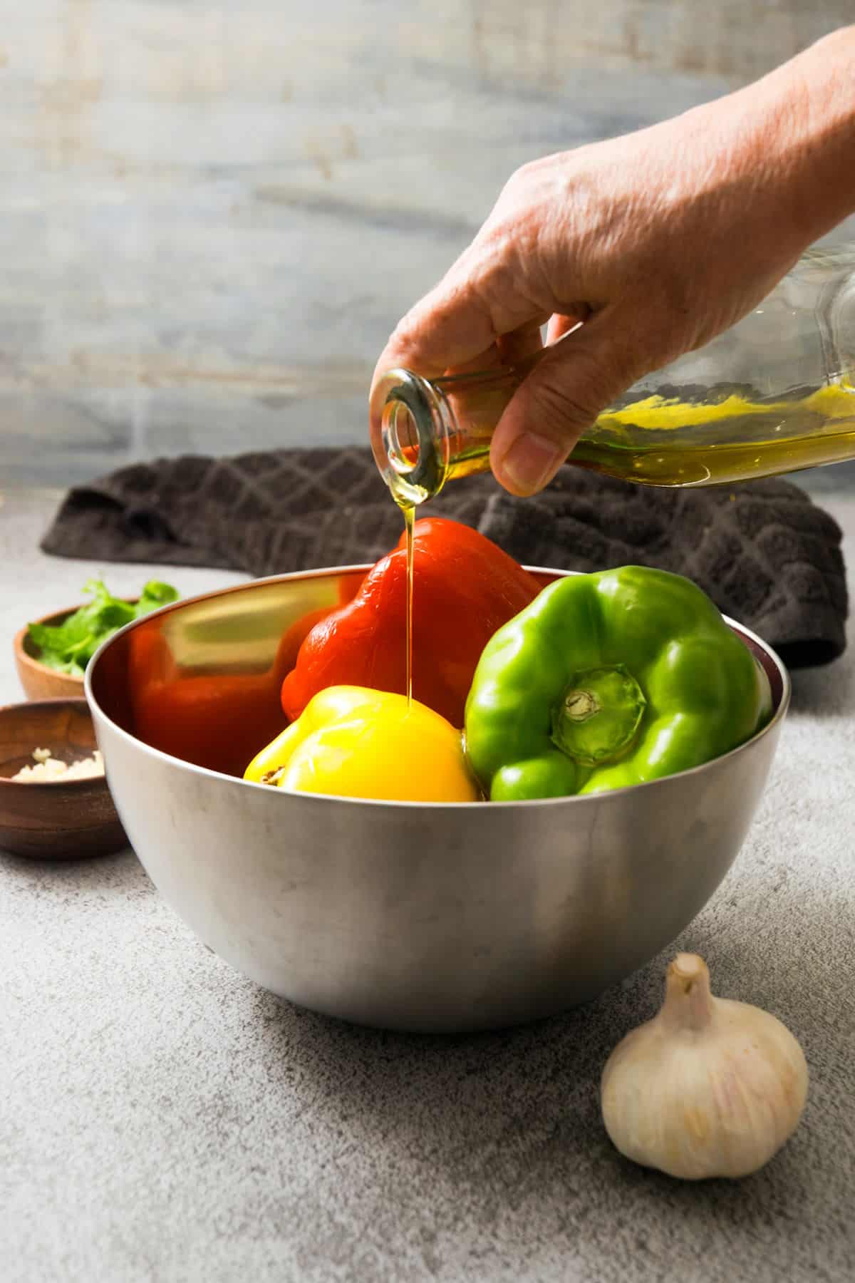 Whole bell peppers in bowl with olive oil.