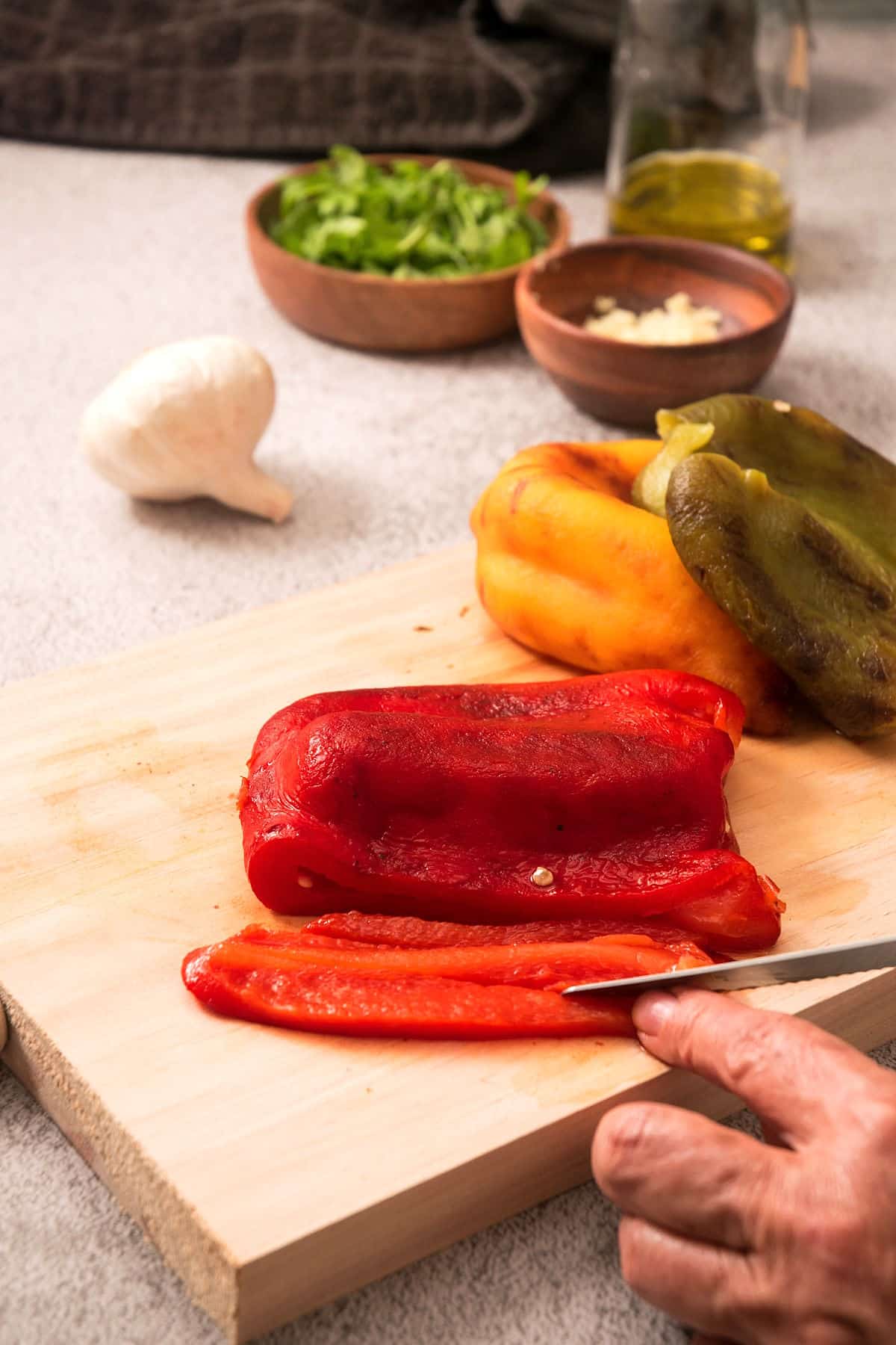 Grilled, peeled peppers on cutting board getting sliced.