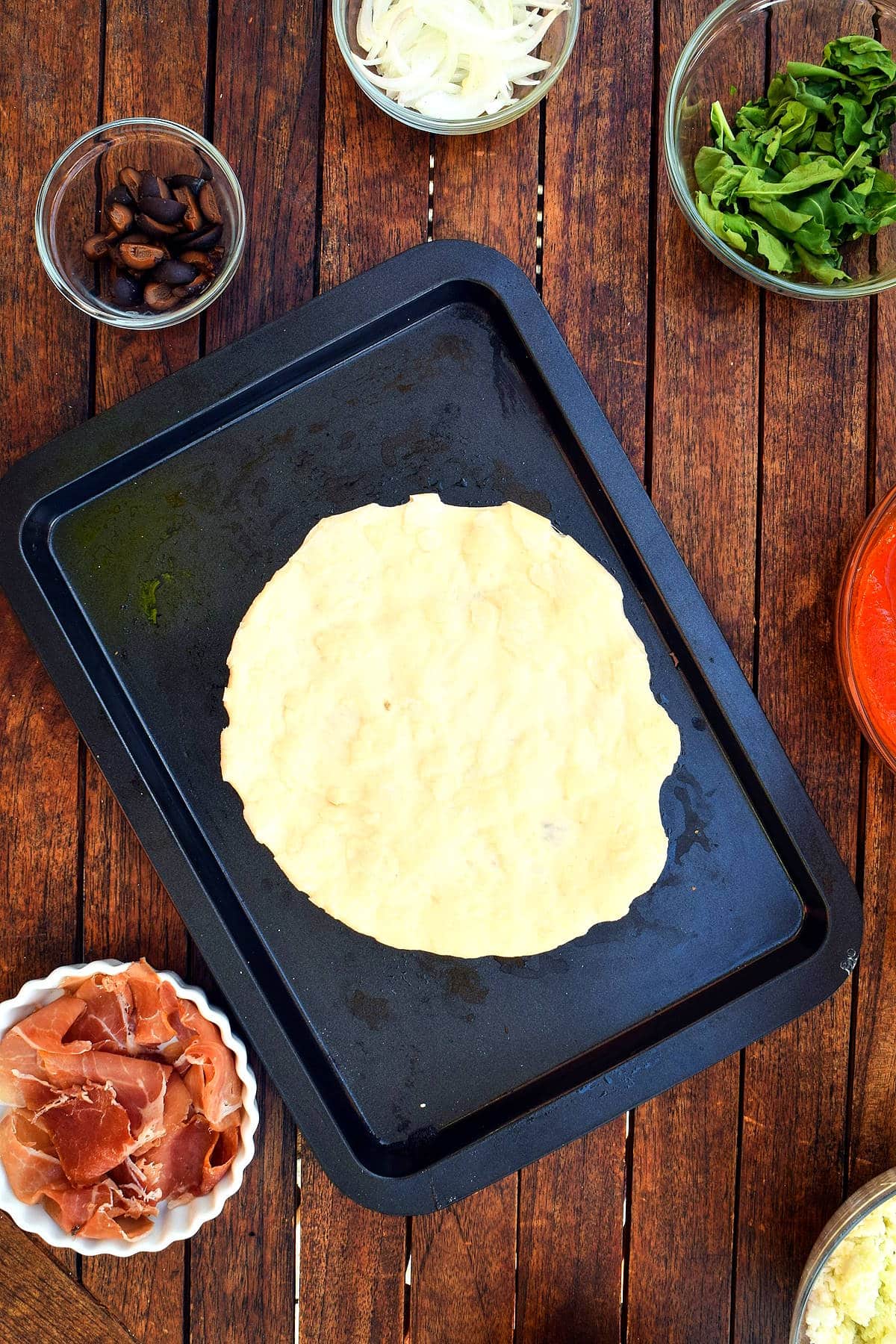 Pizza dough spread out on baking sheet.