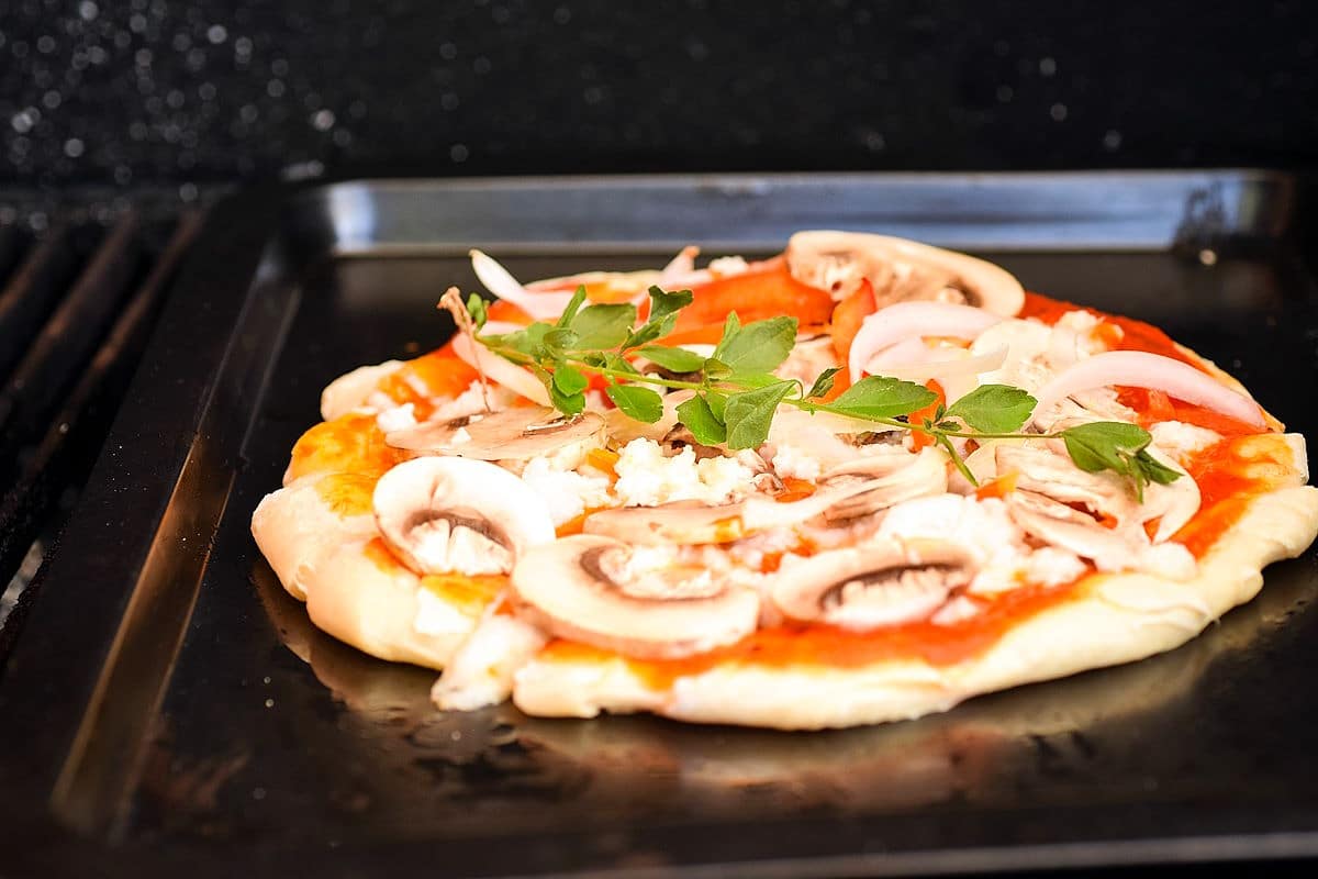 Raw pizza on baking sheet on the grill.