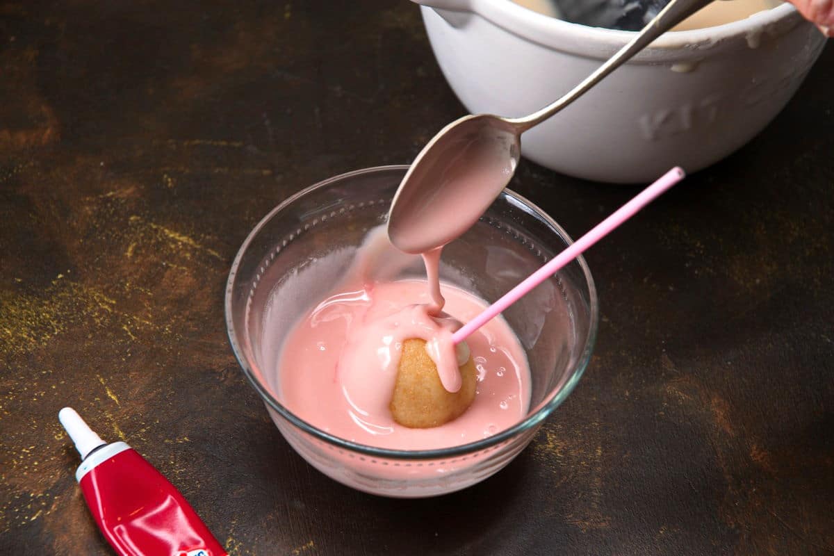 Cake pop getting covered in icing in bowl.