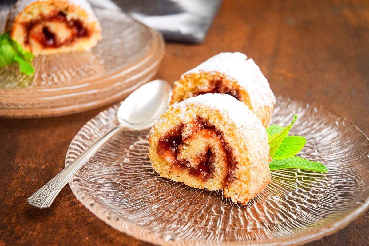 Jelly roll slices on clear, glass dessert plate with icing sugar.