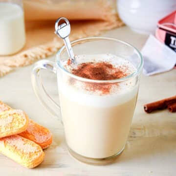 London fog tea latte in a clear glass mug with tea biscuits on the side.