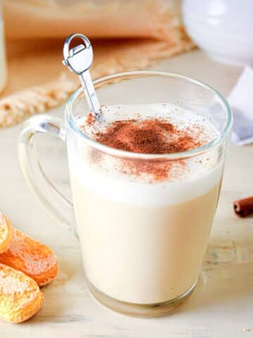 London fog tea latte in a clear glass mug with tea biscuits on the side.