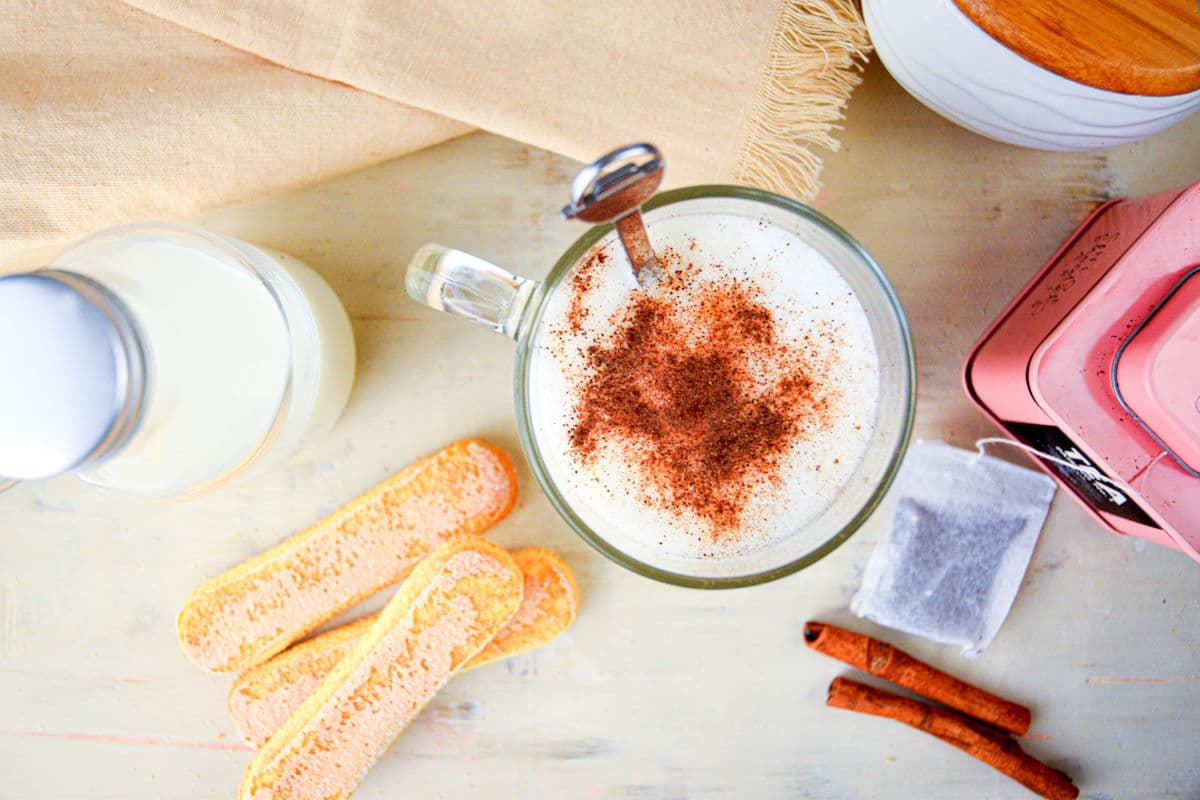 London fog tea latte in mug with tea biscuits and cinnamon sticks on the side.