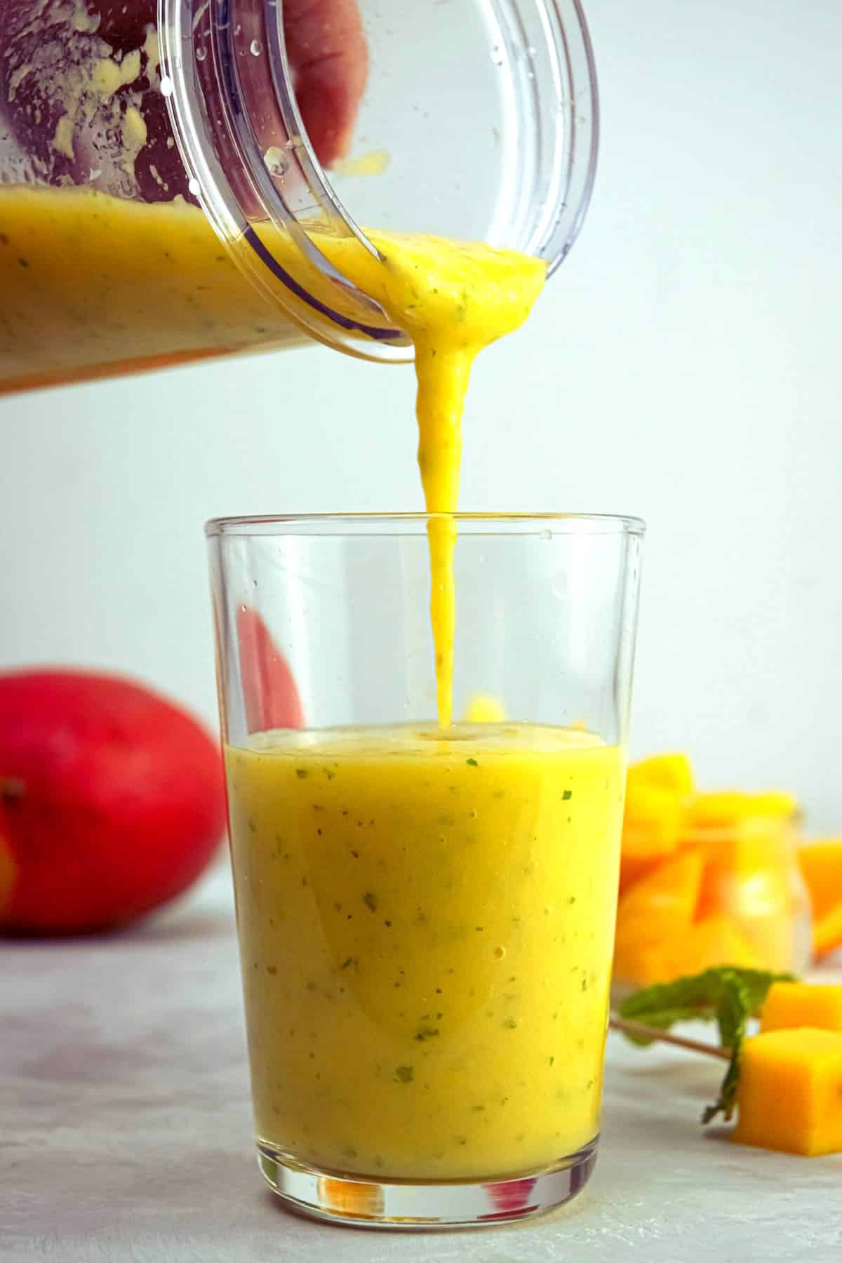 Mango pineapple smoothie pouring into glass.