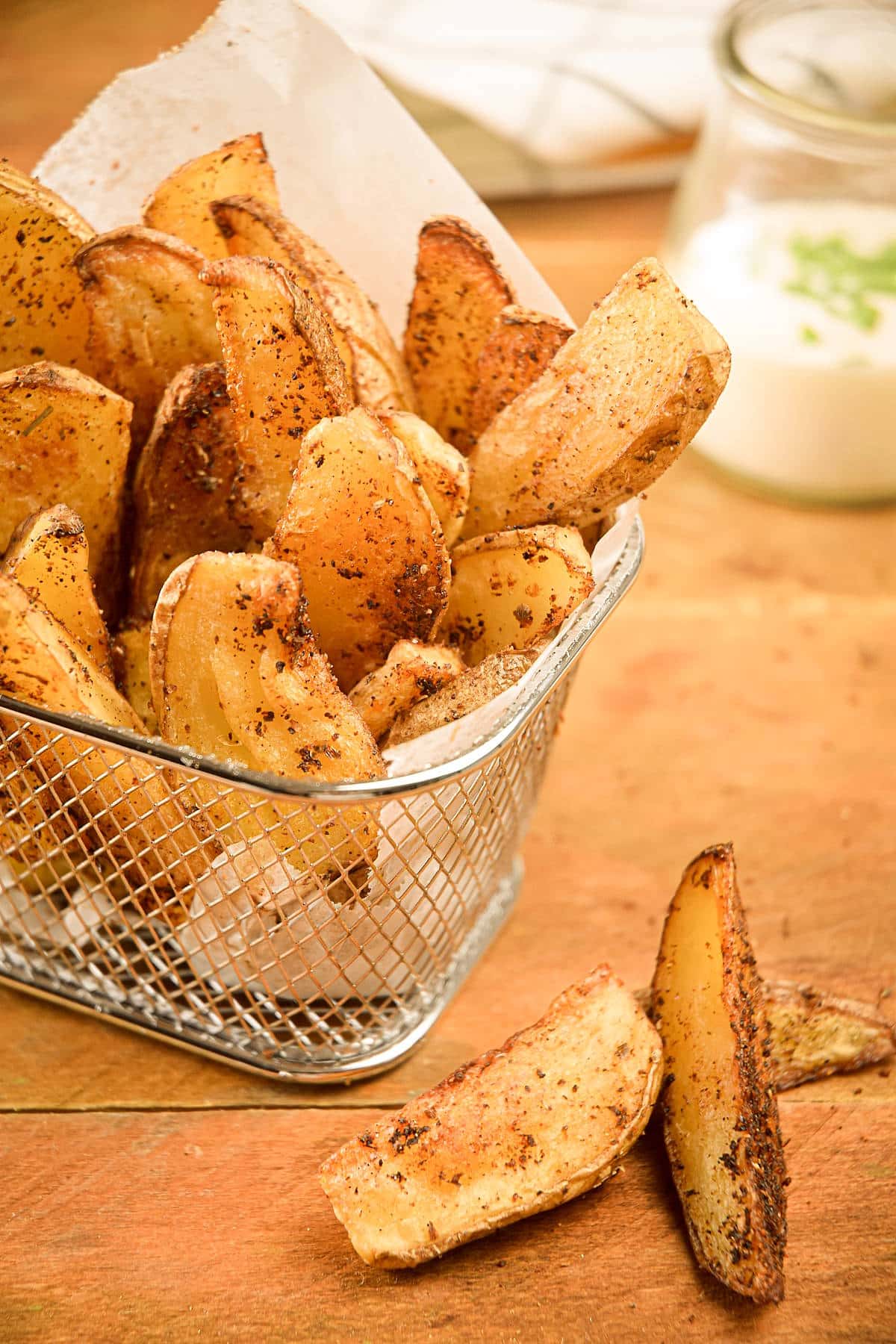 Baked Cajun fries in basket with ranch sauce in the background.
