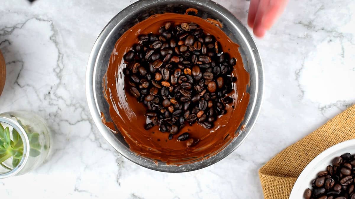 Melted chocolate and coffee beans in metal bowl.