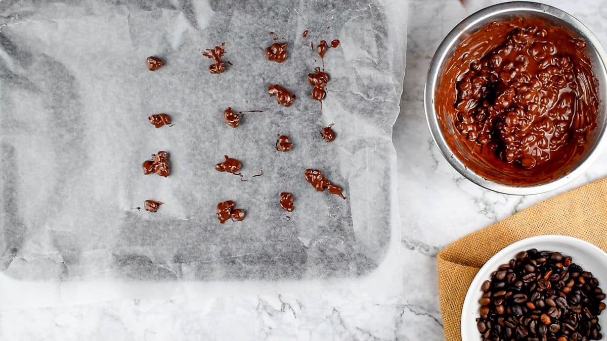 Chocolate covered coffee beans in bowl and on wax paper individually.
