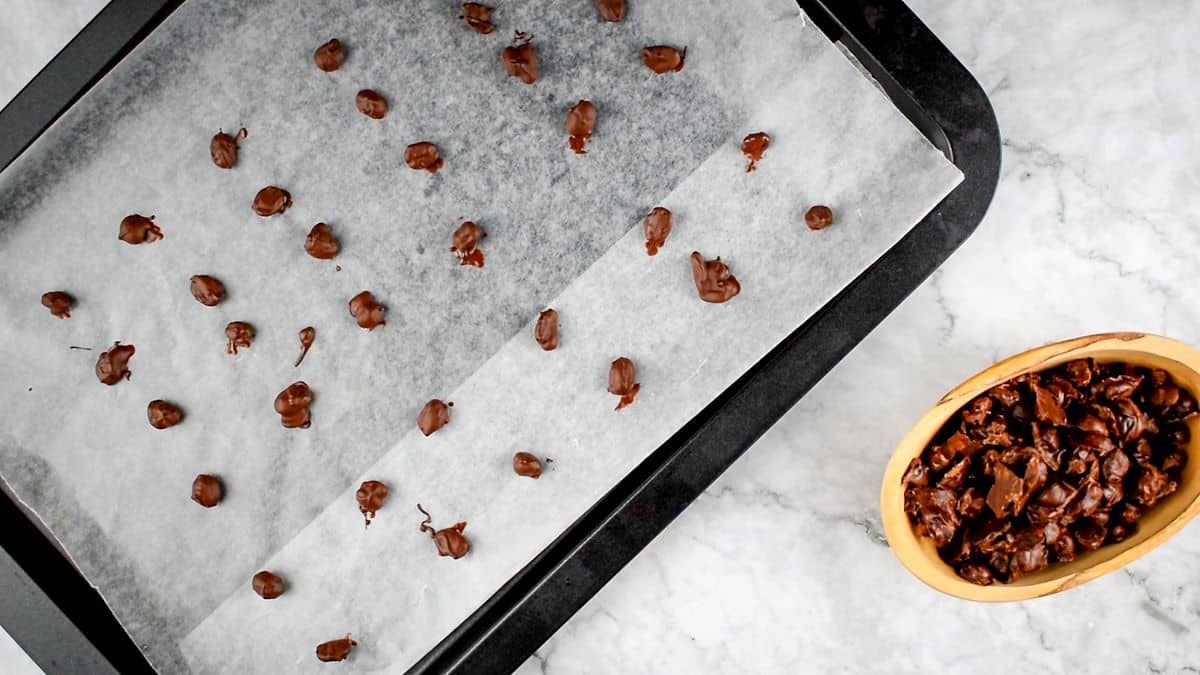 Chocolate covered coffee beans on parchment lined baking sheet.