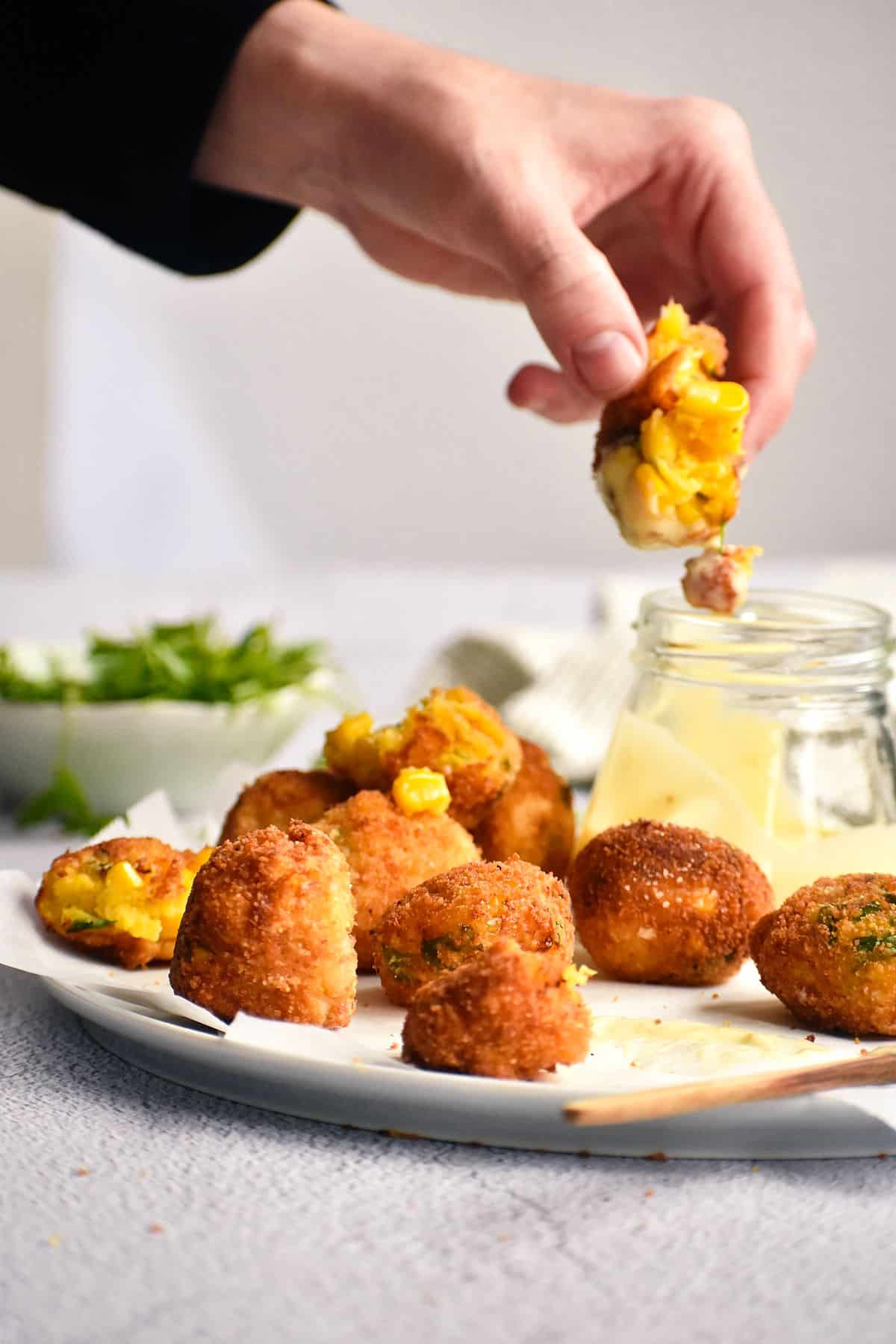 Fried corn nuggets on plate with dip and a woman's hand holding a nugget.