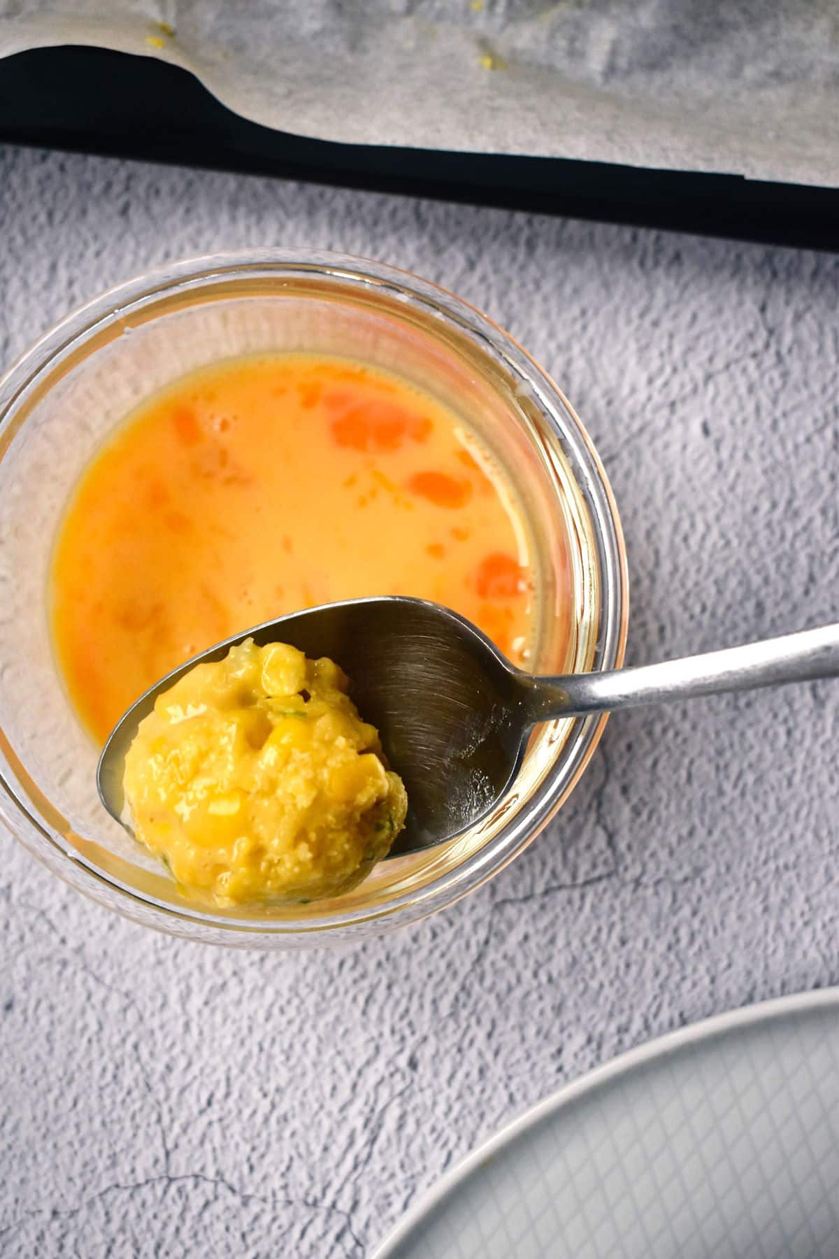 Raw corn nugget dipped in egg mixture on spoon.