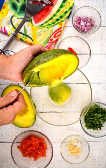 Avocado flesh getting spoon into bowl.