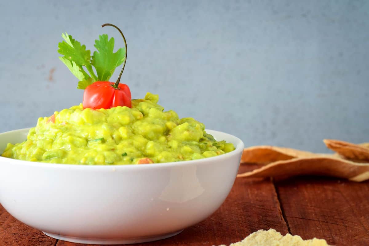 Basic guacamole in white bowl with chili pepper and cilantro on top.