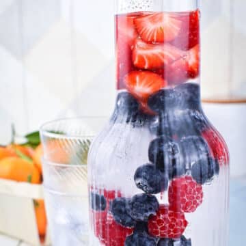 Fruit infused water with berries in glass pitcher.