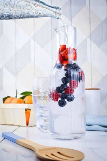 Water pouring into pitcher of fruit.