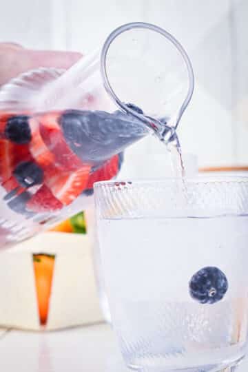 Fruit infused water in pitcher, pouring into glass.