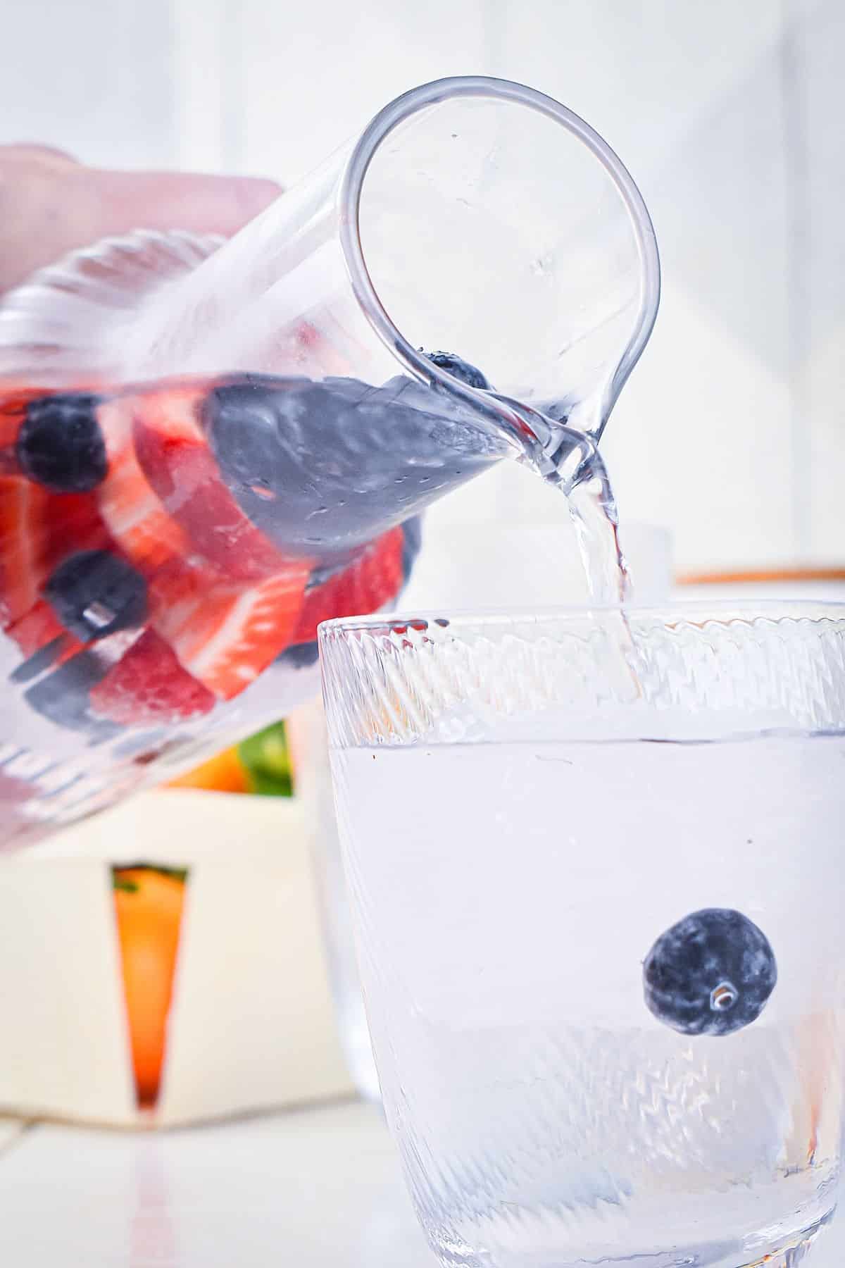 Fruit infused water in pitcher, pouring into glass.