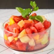 Fruit salad in a glass dish on white tile.