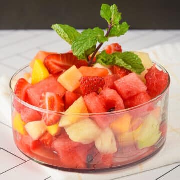 Fruit salad in a glass dish on white tile.