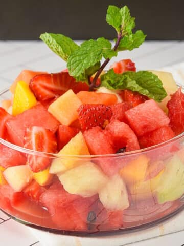 Fruit salad in a glass dish on white tile.