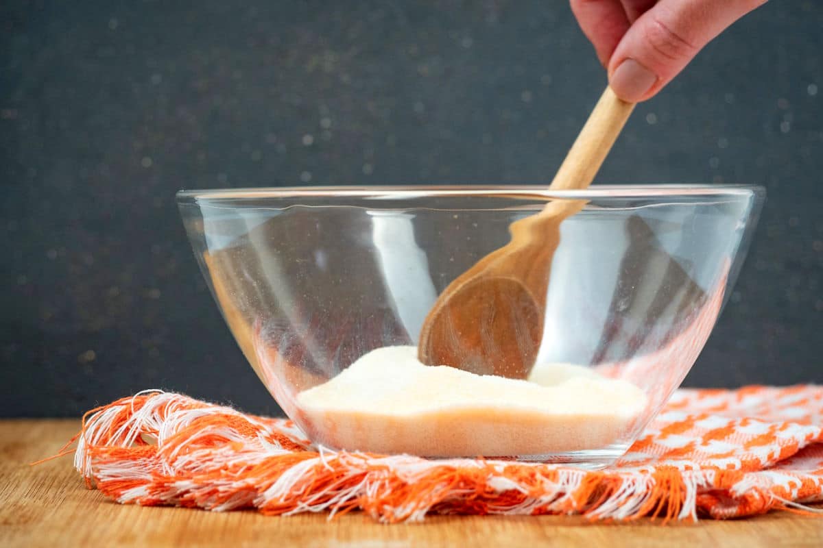 Gelatin and Jello powder in small bowl with wooden spoon.