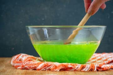 Green Jello powder and warm water in small bowl with wooden spoon.