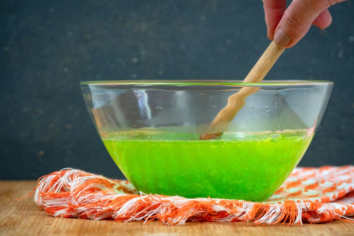 Green Jello powder and warm water in small bowl with wooden spoon.