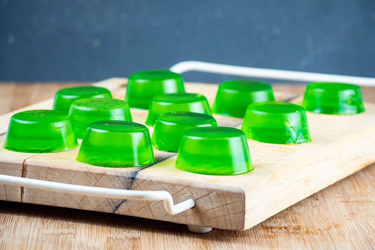 Green homemade gummies on wooden cutting board.