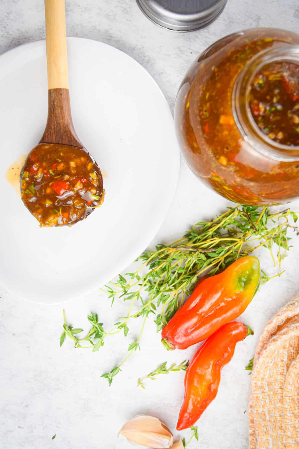 Jark sauce in jar and on spoon with peppers, thyme and garlic on side.