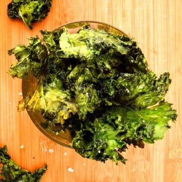 Crispy kale chips in dish on wooden background.