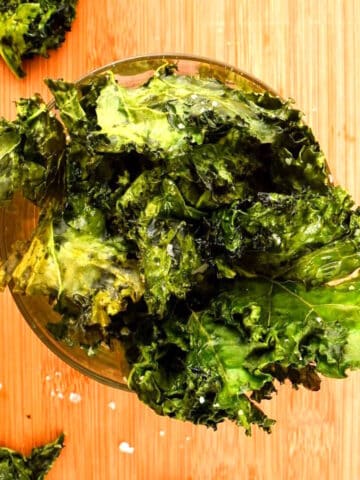 Crispy kale chips in dish on wooden background.