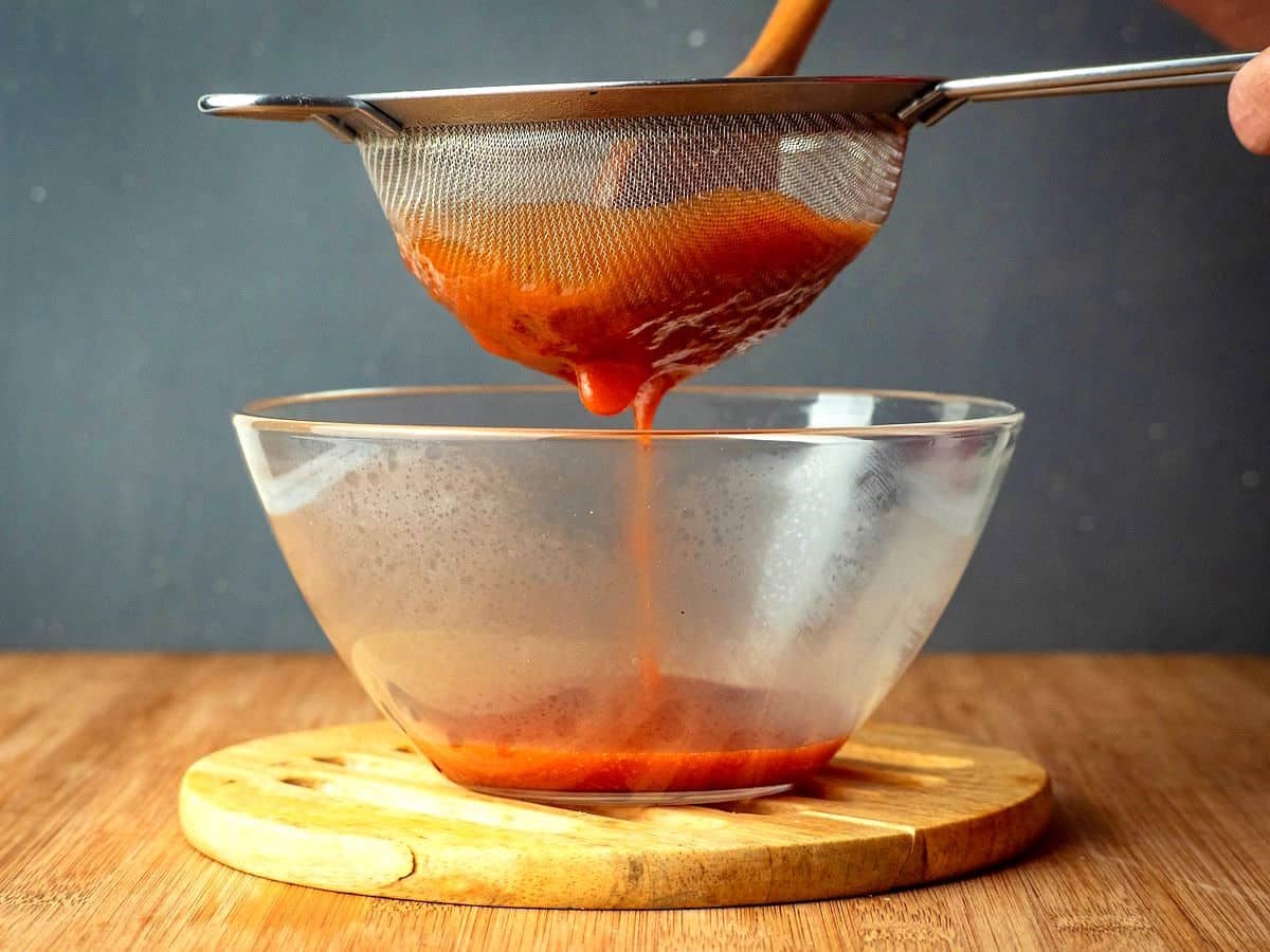 Homemade ketchup straining through mesh strainer.