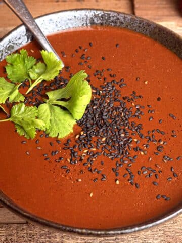 Mole sauce in a bowl with cilantro and black sesame seeds.