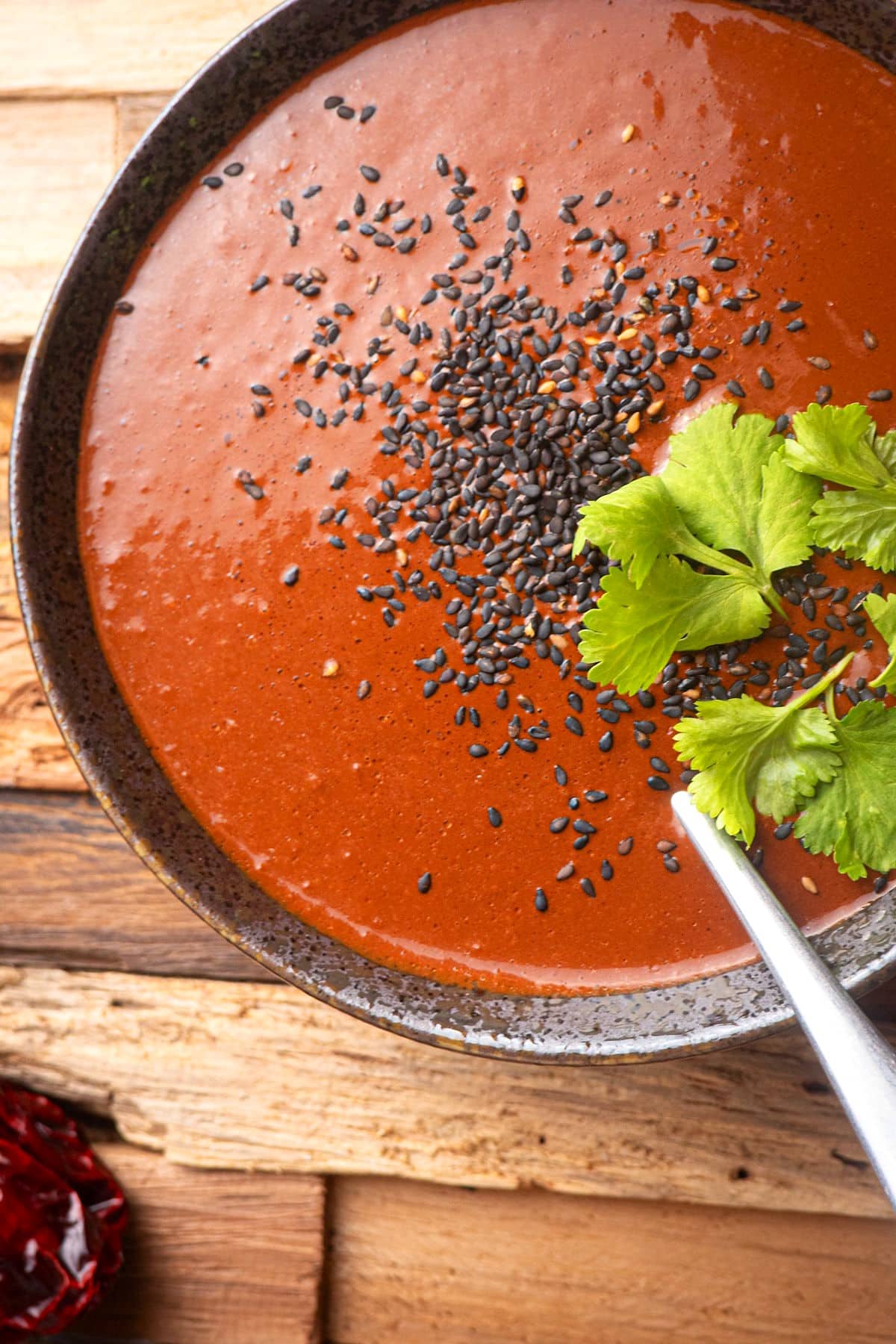 Mole sauce in a bowl with cilantro and black sesame seeds.