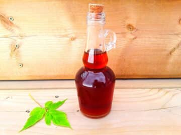 Pure maple syrup in bottle on wooden board with maple leaf beside it.