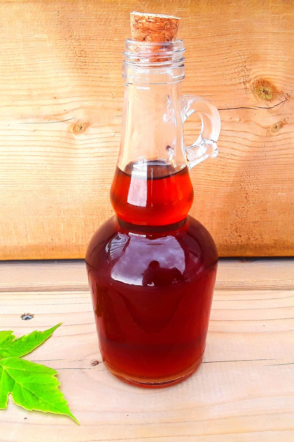 Pure maple syrup in bottle with maple leaf beside it.