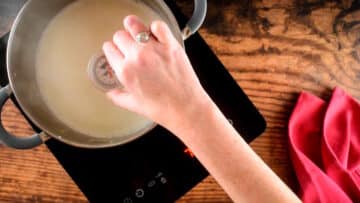 Pot of milk on heating element and thermometer.