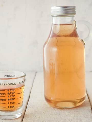 Simple syrup in bottle and small measuring cup.