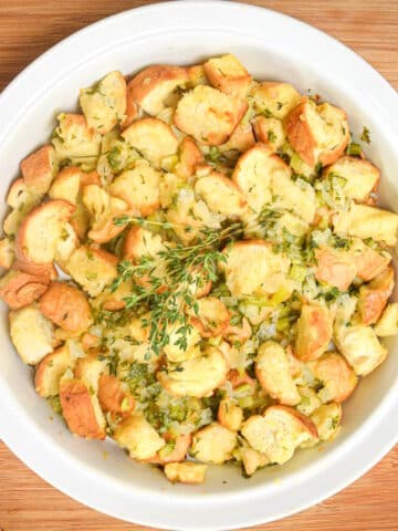 Thanksgiving stuffing/dressing in white bowl with fresh herbs.
