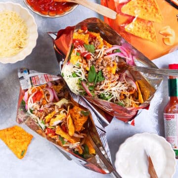 Taco in a bag with forks and toppings on the side.