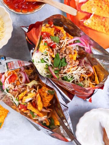 Taco in a bag with forks and toppings on the side.