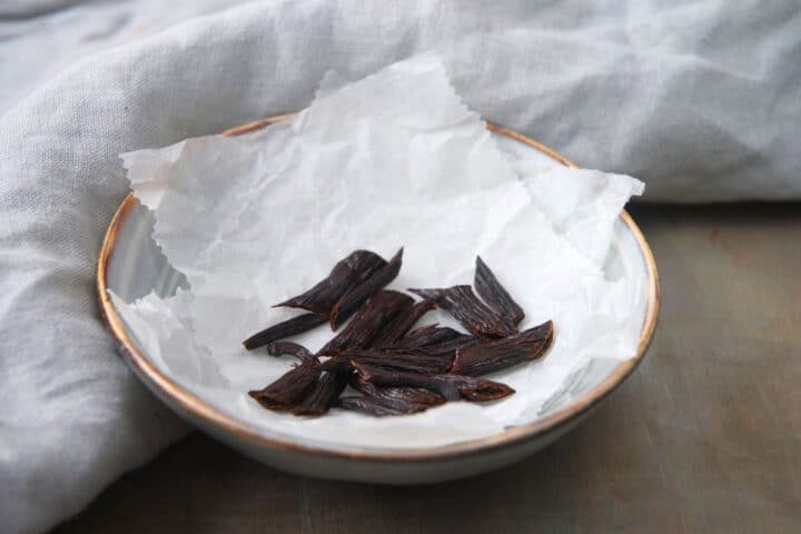 How to Make Vanilla Powder Step 5 Vanilla beans cut into pieces on parchment.