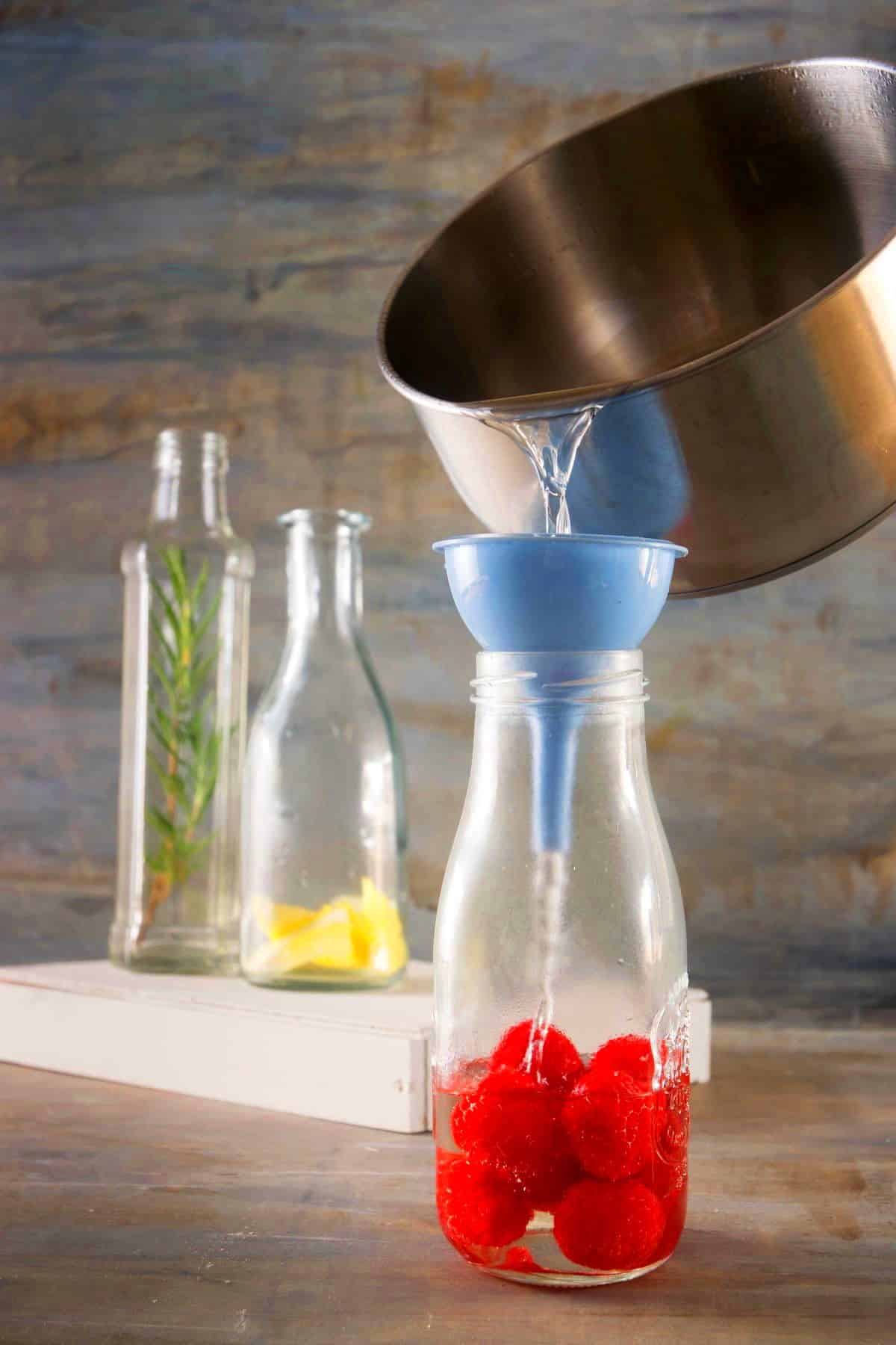 Syrup pouring out of saucepan into jar of raspberries.
