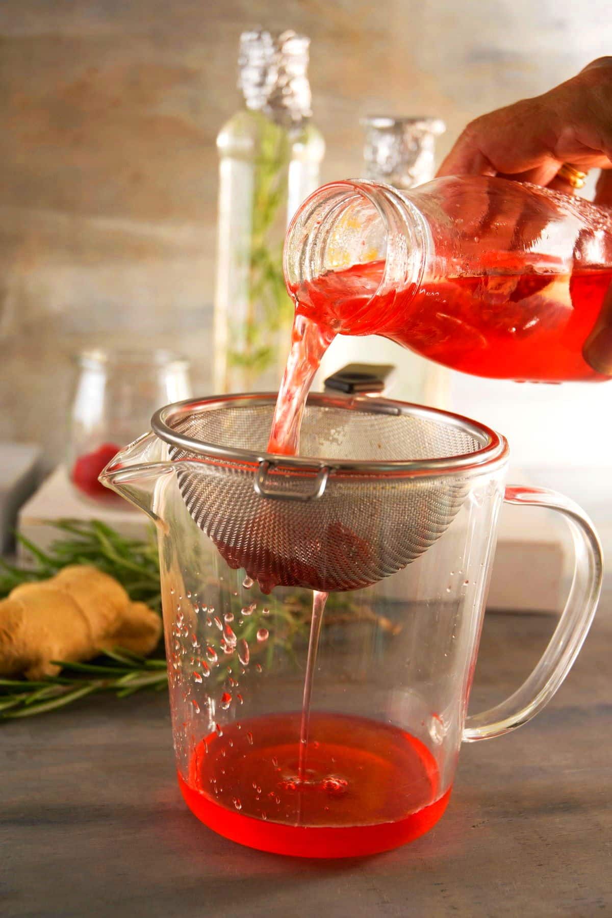 Raspberry cocktail syrup straining through fine mesh strainer.