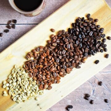 4 colors of coffee beans on wooden board with a mug of coffee on the side.