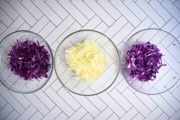 Red and green cabbage shredded on white tile background.