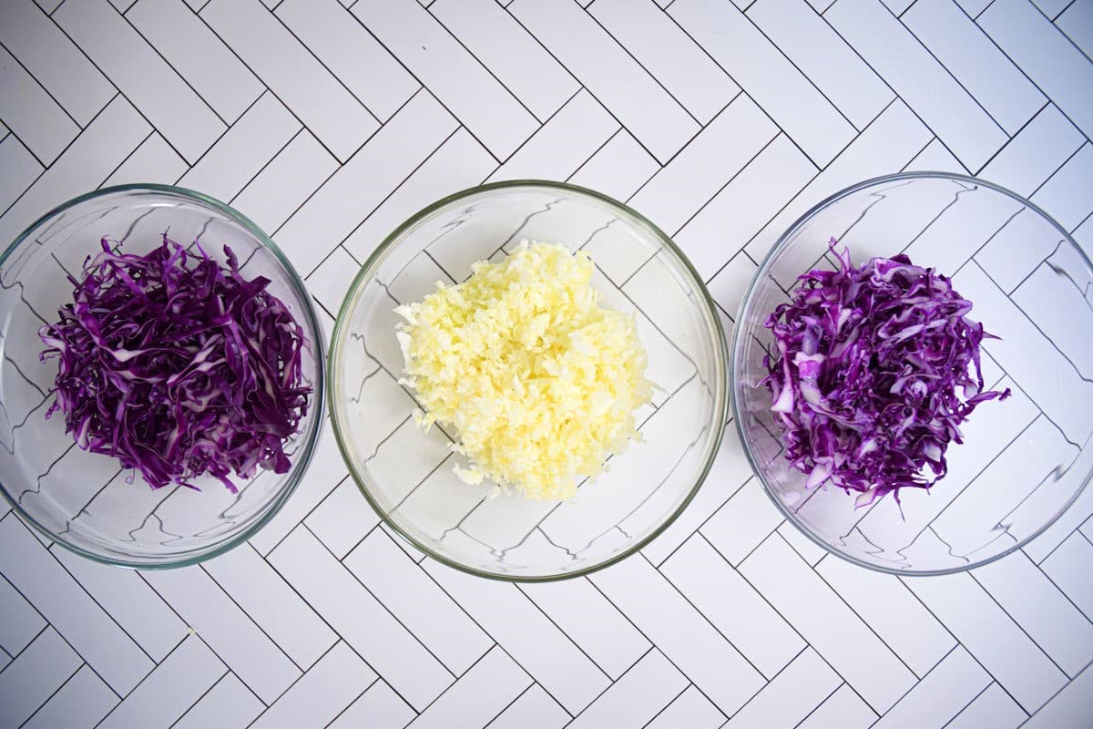 Red and green cabbage shredded on white tile background.