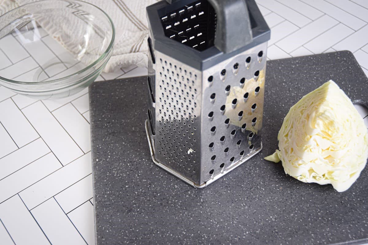 Green cabbage quarter on cutting board with box grater.