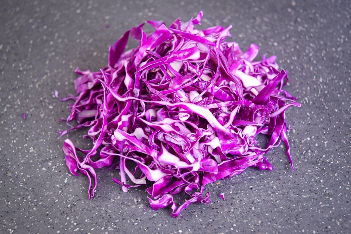 Red cabbage shredded on black cutting board.